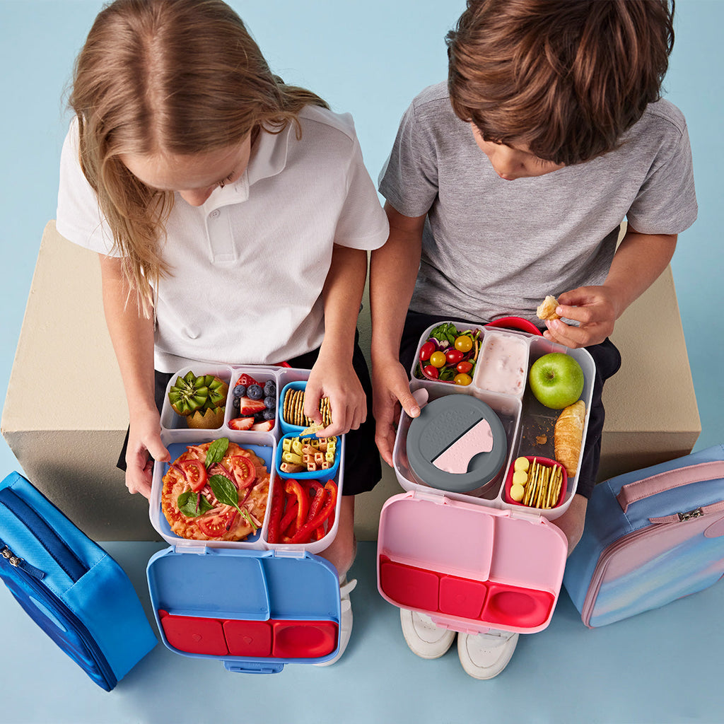 Two children with bbox bento-style lunch boxes filled with food on a light blue background
